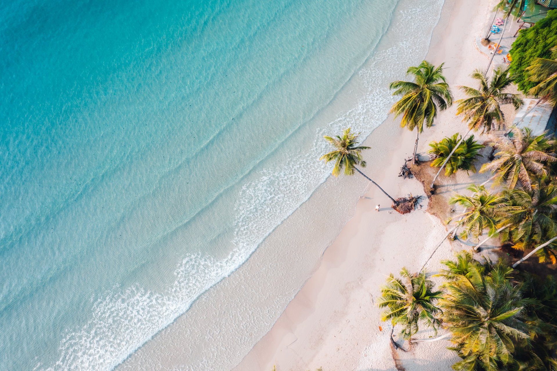 Aerial view of tropical island beach with crystal clear turquoise water and palm trees