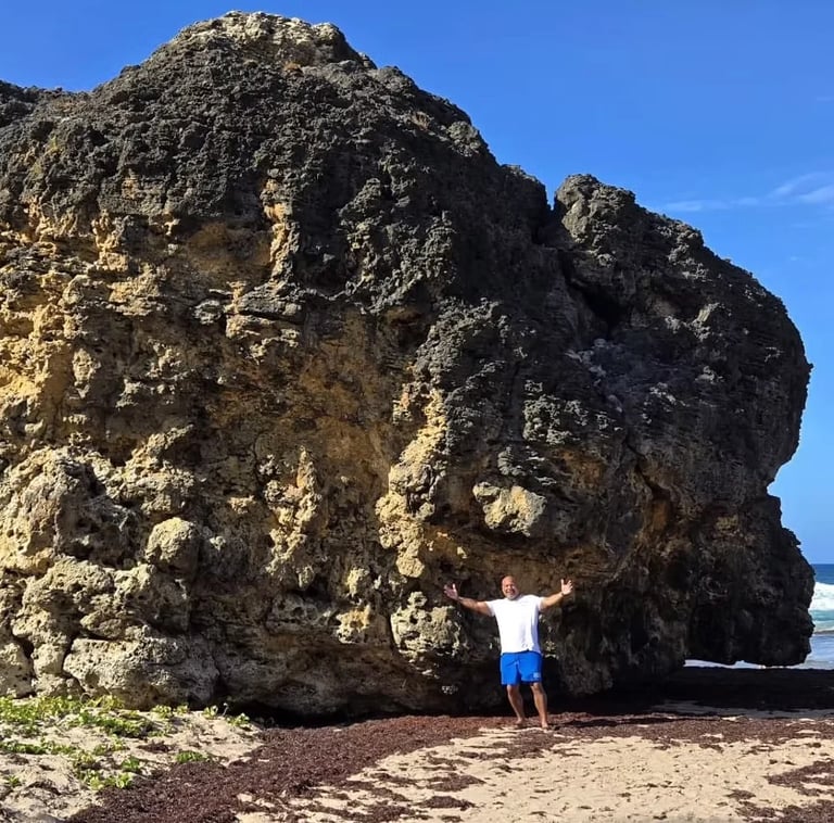 Person standing under a massive rocky cliff on a Barbados beach