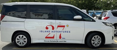 White passenger van with Island Adventures 21 Inc. logo and text, parked in lot with trees