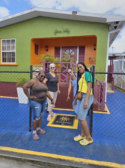Three women standing in front of a colorful lime green and orange house with a blue gate