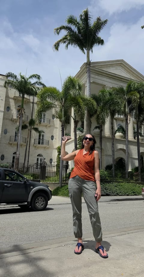 Woman in orange top and khaki pants posing in front of a colonial building with palm trees