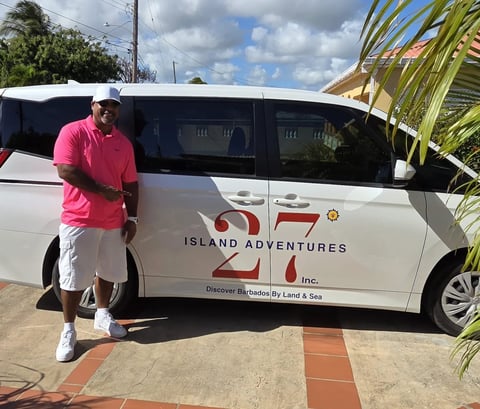 Man in pink shirt standing next to white Island Adventures tour van in tropical setting