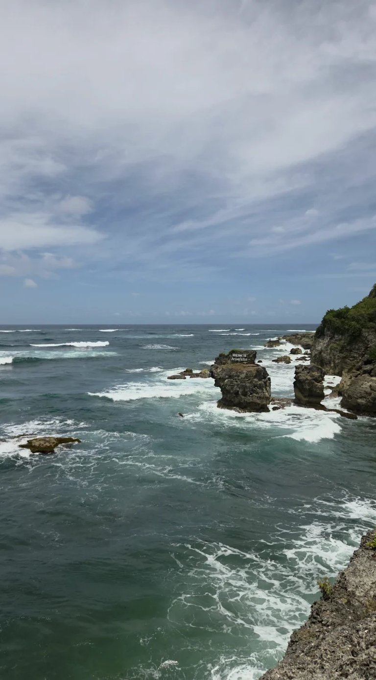 Dramatic rocky coastline with crashing waves and cloudy sky overlooking turquoise ocean waters